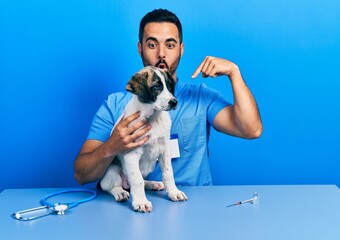 Sticker - Handsome hispanic veterinary man with beard checking dog health pointing down with fingers showing advertisement, surprised face and open mouth