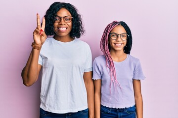 Wall Mural - Beautiful african american mother and daughter wearing casual clothes and glasses showing and pointing up with fingers number two while smiling confident and happy.