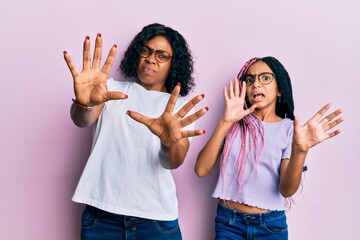 Poster - Beautiful african american mother and daughter wearing casual clothes and glasses afraid and terrified with fear expression stop gesture with hands, shouting in shock. panic concept.