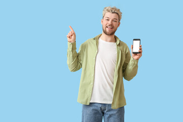 Poster - Young man with mobile phone pointing at something on color background