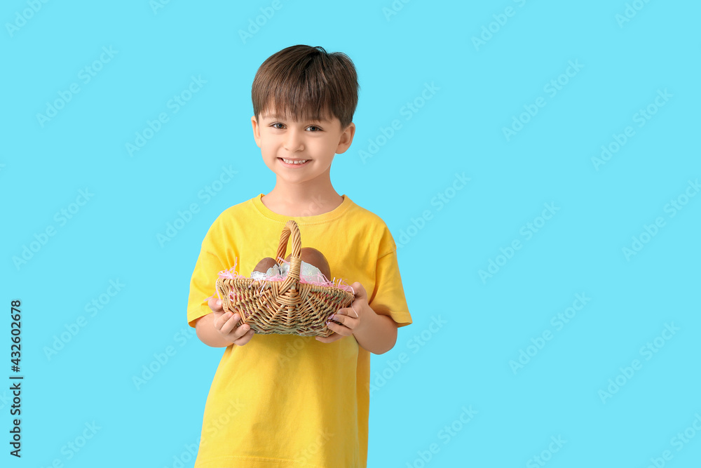 Cute little boy with basket of chocolate Easter eggs on color background