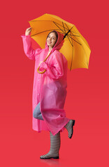 Canvas Print - Stylish young woman in raincoat and with umbrella on color background