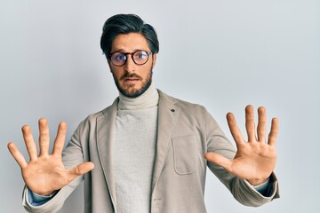 Young hispanic man wearing business jacket and glasses afraid and terrified with fear expression stop gesture with hands, shouting in shock. panic concept.