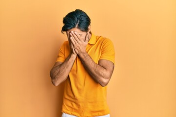 Young hispanic man wearing casual yellow t shirt with sad expression covering face with hands while crying. depression concept.