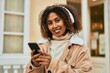© Krakenimages.com - Young african american woman smiling happy using smartphone and headphones at the city.