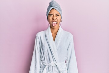 Poster - Young chinese woman wearing shower towel cap and bathrobe sticking tongue out happy with funny expression. emotion concept.