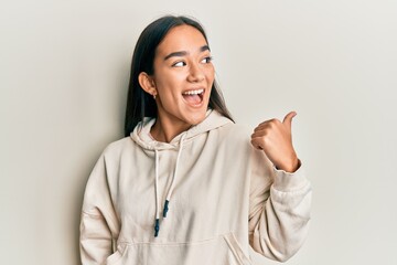 Poster - Young asian woman wearing casual sweatshirt pointing thumb up to the side smiling happy with open mouth