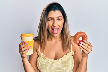 Sticker - Beautiful brunette woman eating doughnut and drinking coffee winking looking at the camera with sexy expression, cheerful and happy face.