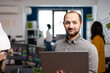 © DC Studio - Video editor worker standing in front of camera smiling working in creative agency office holding laptop. Man videographer works in multimedia studio production editing video in modern workplace.