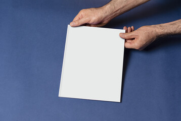 Poster - Closeup shot of a male hand holding a closed book-catalog with a blank cover on blue background