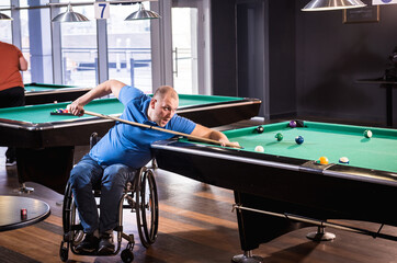 Adult man with disability in a wheelchair play billiards in the club