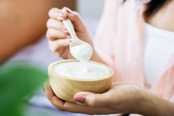 closeup woman hand eating yogurt hand holding wooden spoon and bowl of yogurts