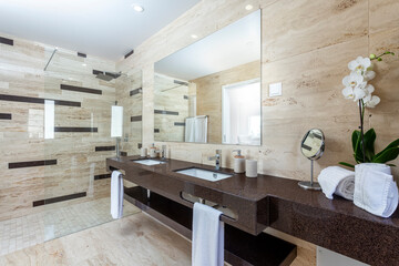 Modern tiled gray bathroom of a resort, with a sink facing a toilet and a shower at the end of the room.