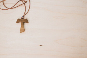 Top view of a wooden tau cross necklace on a wooden surface for a copy space