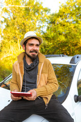 Latino traveler man with sombrero sitting on the hood of his car and using modern technology to chart the route of his trip using gps. Adventure and off-road routes. joyride.