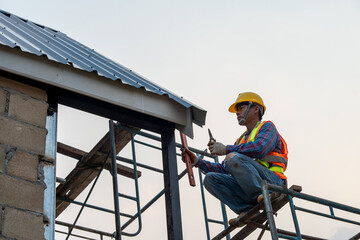 Poster - Roofer worker in protective uniform wear and gloves,Roofing tools,installing new roofs under construction,Electric drill used on new roofs with metal sheet.