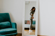 © shevtsovy - Fitness Woman Measuring body With Tape Standing In Front Of Mirror At Home. Beautiful woman checking success of weight loss program and measuring butt and hips in front of mirror in living room