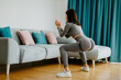 © shevtsovy - female butt workout squats at home. Athletic Woman squats workout in living room. Female gymnastics. Glutes workout motivation. Fitness at home concept.