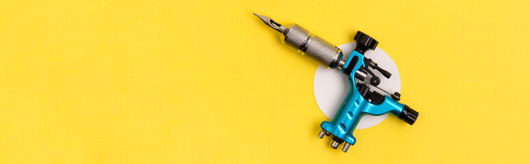 Blue tattoo machine on yellow background. Tattooing artist studio minimal layout