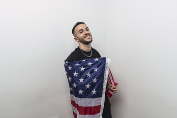 Poster - Young handsome Spanish male wrapped in an American flag posing isolated on a white background