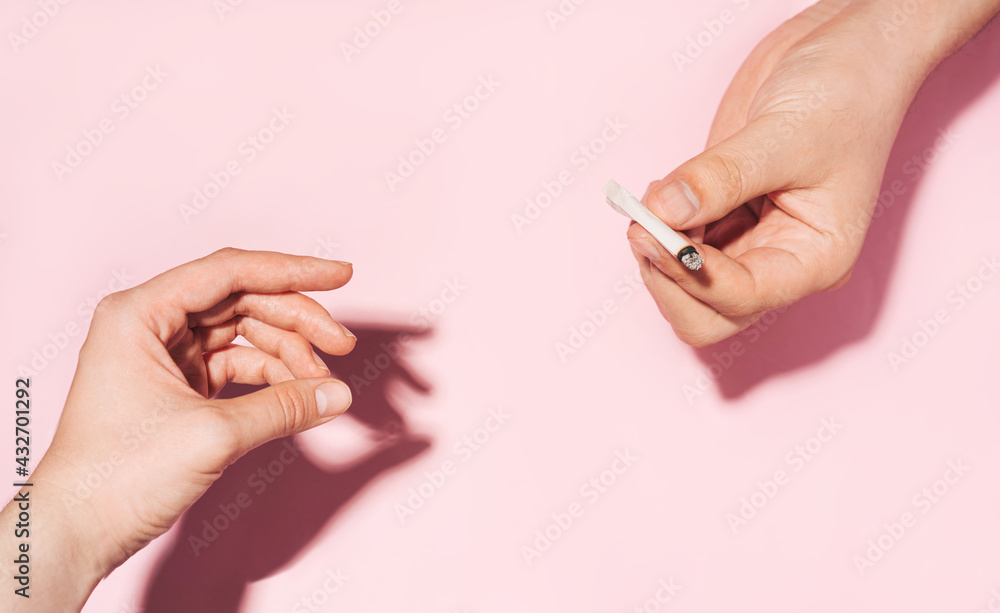 Passing cannabis cigarette from hand to hand. Cannabis smoking concept.  pastel colour photo of Hands giving each other smoldering paper cigarette  Stock Photo