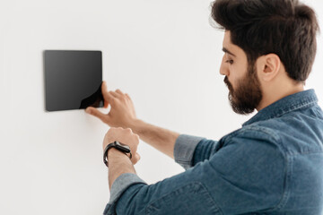Poster - Arab guy using thermostat smart home domotic control panel on wall for house temperature
