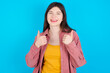 Optimistic young beautiful Caucasian woman wearing pink jacket over blue wall showing thumbs up with positive emotions. Quality and recommendation concept.