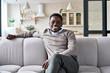 © insta_photos - Young adult happy cheerful smiling African American business man with toothy smile relaxing posing sitting on comfortable sofa at home modern living room looking at camera. Work life balance concept.