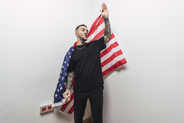 Wall Mural - Happy Spanish male with tattooed arms posing with an American flag isolated on a white background