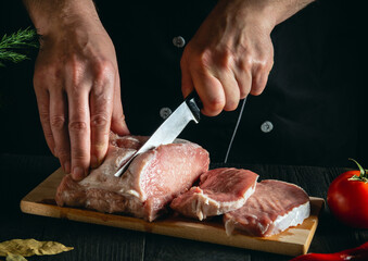 Chef or cook cutting meat with knife on kitchen, cooking food. Vegetables and spices on the kitchen table to prepare a delicious lunch