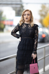 Poster - Blonde female posing in an elegant black evening dress holding a pink bag