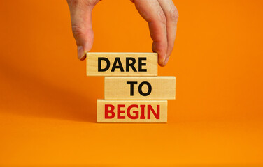 Dare to begin symbol. Wooden blocks with words 'Dare to begin'. Beautiful orange background, businessman hand. Business, dare to begin concept, copy space.