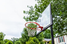 Closeup Of Red Basketball Hoop With Net And Glass Board In Playground Looking Up At Sky And House In Background
