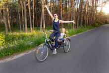 Young Adult Caucasian Mom Enjoy Having Leisure Fun Riding Bicycle With Cute Adorable Blond Daughter Holding Wild Field Flower At Scenic Rural Country Road On Bright Sunny Day. Countryside Vacation