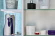 Oral irrigator and other personal hygiene items are located on shelves of wall cabinet in bathroom.
