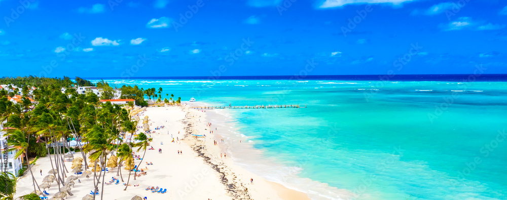 Beach vacation. Aerial drone view of tropical white sandy Bavaro beach in Punta Cana, Dominican Republic. Amazing landscape with palms, umbrellas and turquoise water of atlantic ocean. Wide format - obrazy, fototapety, plakaty 