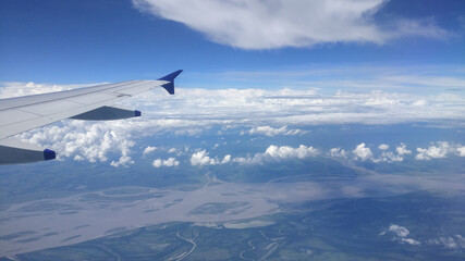 Dramatic cumulus clouds and an aerial view of the Brahmaputra delta captured from the window of a flying airplane with one of its wings in sight.