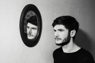 Wall Mural - Black and white photo; portrait of young man near his reflection in mirror.