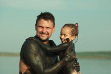 Therapeutic Mud For The Body. Mud Baths On The Lake. A Man And A Child Are Smeared With Clay. Family At The Resort