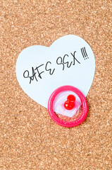 Safe sex message and condom with pin on wooden board for reminder.