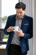 © Bangkok Click Studio - Portrait of smart confident young businessman in modish blue suit sitting on desk in the office, holding a cup of coffee.