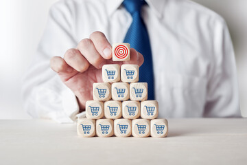 Wall Mural - Businessman placing cube with target symbol on top of tiered wooden cubes with shopping cart icon.