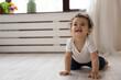 Smiling small African American toddler girl child crawl on wooden floor at home explore house apartment. Happy little ethnic biracial baby kid have fun play laughing. Childcare, parenting concept.