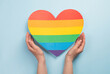 Womans hands hold heart in the colors of rainbow on light blue background. LGBT concept, Pride month. Top view