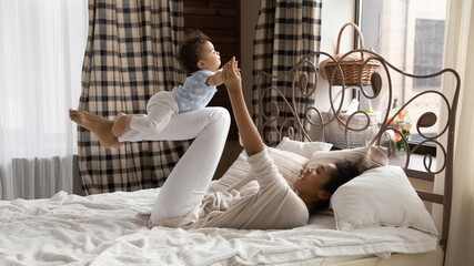 Wall Mural - caring happy young african american mom lying in bed have fun play with cute little baby girl child.