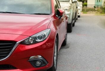 Closeup of front side of red  car with  other cars parking in outdoor parking area.