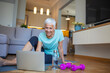 © Dragana Gordic - Senior woman sitting on the floor on exercise mat in front of laptop and training at home. Beautiful senior woman doing stretching exercise while sitting on yoga mat at home.