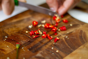 Wall Mural - Closeup shot of hands chopping chili pepper on a wooden food board