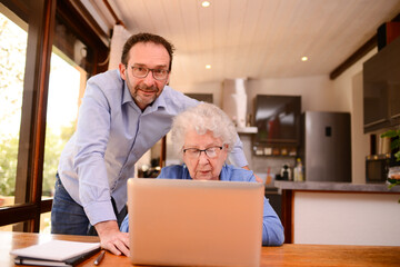 mature man helping elderly senior woman at home with paperwork and computer internet lesson