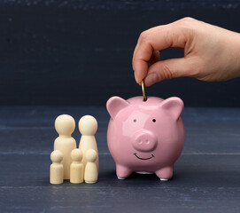 wooden family figurines and pink ceramic piggy bank on blue background